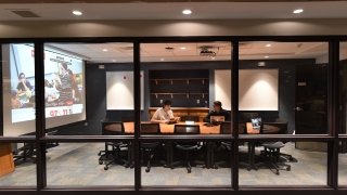 Two students sit at a large conference table in a windowed vestibule in the library.
