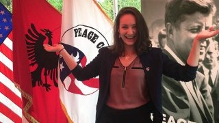 A Saint Lawrence student stands in front of the U.S. flag and the Peace Corps flag.