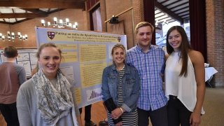 Four students stand in front of a project poster representing their collaborative research.