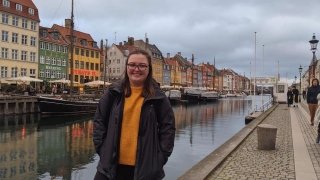A student stands in front of a canal lined with old houses in Copenhagen. 