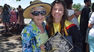 A recent graduate holds their decorated grad cap and smiles for a photo with her grandmother.
