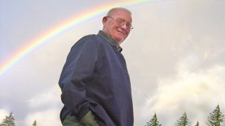 Don Leet stands with a double rainbow in the sky behind him