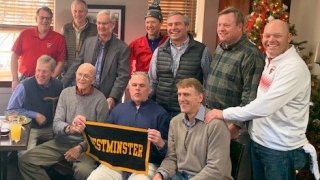 on Leet is seated with a group of ten of his former athletes. A Westminster banner is held.