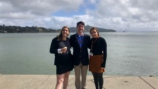 Three students wearing business attire stand in front of a bay on a boardwalk.
