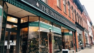 Looking up the street at brick buildings and storefronts, decorated for the holidays, on a Main Street in Canton, N.Y.