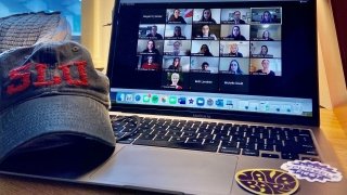 A hat with the letters S, L, U on it next to an open laptop displaying a group of people participating in a networking events.
