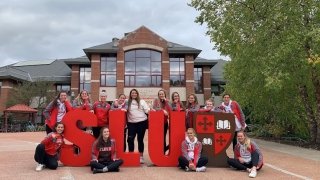 The Saint Lawrence volleyball team gathers around foam letters that spell out "SLU" in front of the Student Center.
