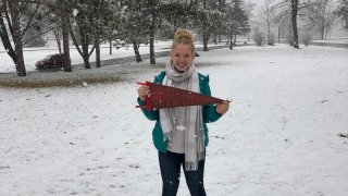 Abbie Cooper, holding a Saint Lawrence University pennant, stands in the snow in Canton, N.Y.
