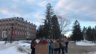 A group of Saint Lawrence students, holding cardboard signs, march on campus. There is snow on the ground.
