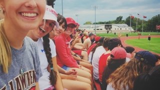 Saint Lawrence students, wearing Saint Lawrence t-shirts and hats, attend a football game. 