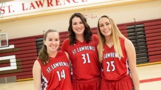 Kaelyn Kohlasch and two fellow members of the Saints women's basketball team, wearing red jerseys on the basketball court. 