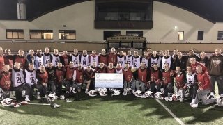 The men's lacrosse team stands together on the field with a check.