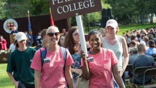 Two Saint Lawrence orientation leaders, holding a sign, lead a group of new Saint Lawrence students. 