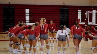 Members of the Saint Lawrence University volleyball team, wearing red jerseys, gather on the court in a circle.