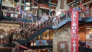 About 70 Saint Lawrence students wearing masks cheer together on a large staircase with a "Welcome Class of 2025" banner draping down from the top floor.
