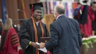 A mentor congratulates and shakes hands with a student at Commencement.