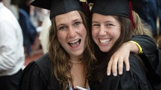 Two graduates smile and look at the camera in excitement.
