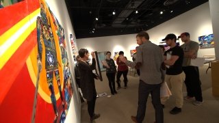 A group of Saint Lawrence University students gather around artwork in the Brush Art Gallery. There is a vibrant red, yellow, and blue painting on the wall. 