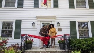 Hagi Bradley, President Kate Morris, and Diamond McAllister cut a big red ribbon on the front porch of a white two-story home with green shutters.