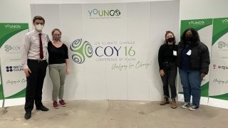 Elise Pierson, and three other delegates, stand in front of a youth climate change conference promotional sign.