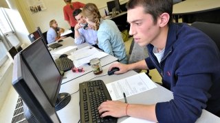 A Saint Lawrence University student uses a computer. A professor collaborates with a student in the background. 