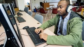 A student, wearing headphones and a green jacket, uses a computer at Saint Lawrence University. 