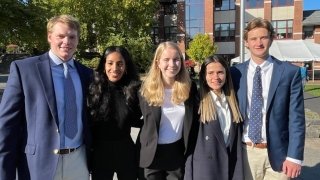 Five students in business attire with their arms around one another in front of the student center on a sunny day on the Saint Lawrence University campus.