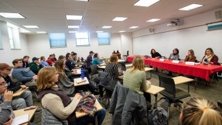A group of sophomore students sit at desks in a large classroom listening to a career preparedness panel of faculty, staff, and alumni. 