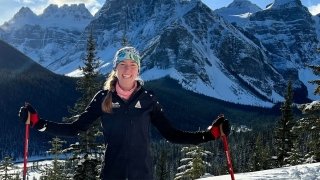Lucy Hochschartner '20 wearing Nordic ski apparel and standing on a snowy peak overlooking the Canadian Rocky Mountains.