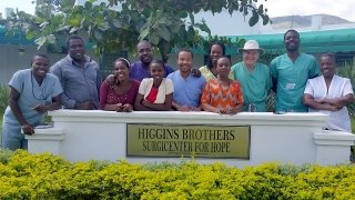 A photo of Ted Higgins and peers smiling around the sign to the Higgins Brothers Surgicenter for Hope