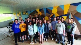 A photo of St Lawrence and Canton Central School students outside of a vibrantly colored mural.