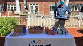 St Lawrence alumni Conor McDermott standing at a table full of snacks and drinks outside the brick wall entrance of Kind Senior Care, a nonmedical home care business.