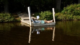 A photo of a student reading on a wooden deck next to a lake.