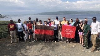 A photo of St Lawrence students and partners in Kenya standing in front of a picturesque lake holding St Lawrence flags.