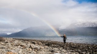 A photo of St Lawrence student on the beach with a half of the rainbow in the sky looking like the end is on the student's palm.