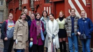 A group of students in warm clothing stand in front of a red and white building in Rennes, France.