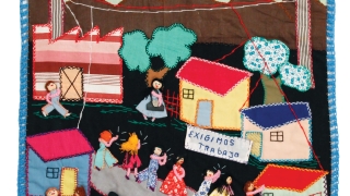 A photo of an arpillera that features brightly colored houses and people.