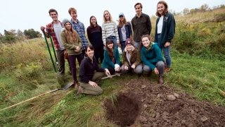 A photo of Ceramics 1 students posing in a field behind a large hole they dug.