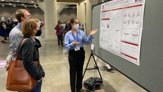 A student explains their research poster to conference attendees.
