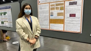 A student stands in front of their research project at a conference.