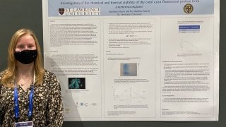 A student stands in front of their research project at a conference.