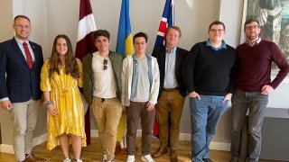 Saint Lawrence students, studying abroad in London, stand in front of the flags of Latvia, Ukraine, and the United Kingdom at the Embassy of Latvia in London, England.