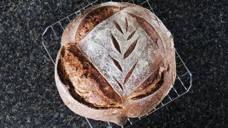 A close up photo of a freshly baked loaf of bread with a leaf design cut into the top.