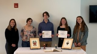 five students standing behind a table while two of those students hold their Tri-Beta membership certificates