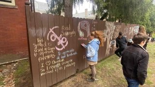 Sara Ashpole stands outside on a sunny day and draws on a brown fence with chalk.