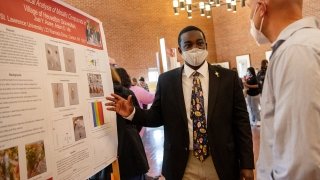 A student stands next to a large research poster and explains their project to a Festival Day attendee.