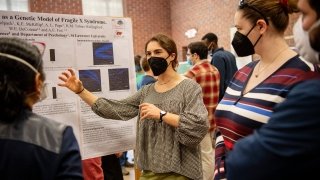 A student enthusiastically explains the results of their research project as several attendees listen in.