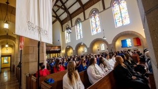 The pews of Gunnison Memorial Chapel are filled with students wearing white, red, black, and blue robes.