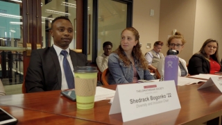Shedrack Bogonko '22 sits at a glossy conference table, wearing a suit and tie, during a student government meeting.