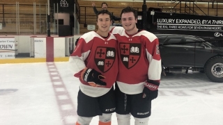 Tommy Benjes puts his arm around a teammate. They're standing on an ice rink and wearing Saint Lawrence hockey uniforms.